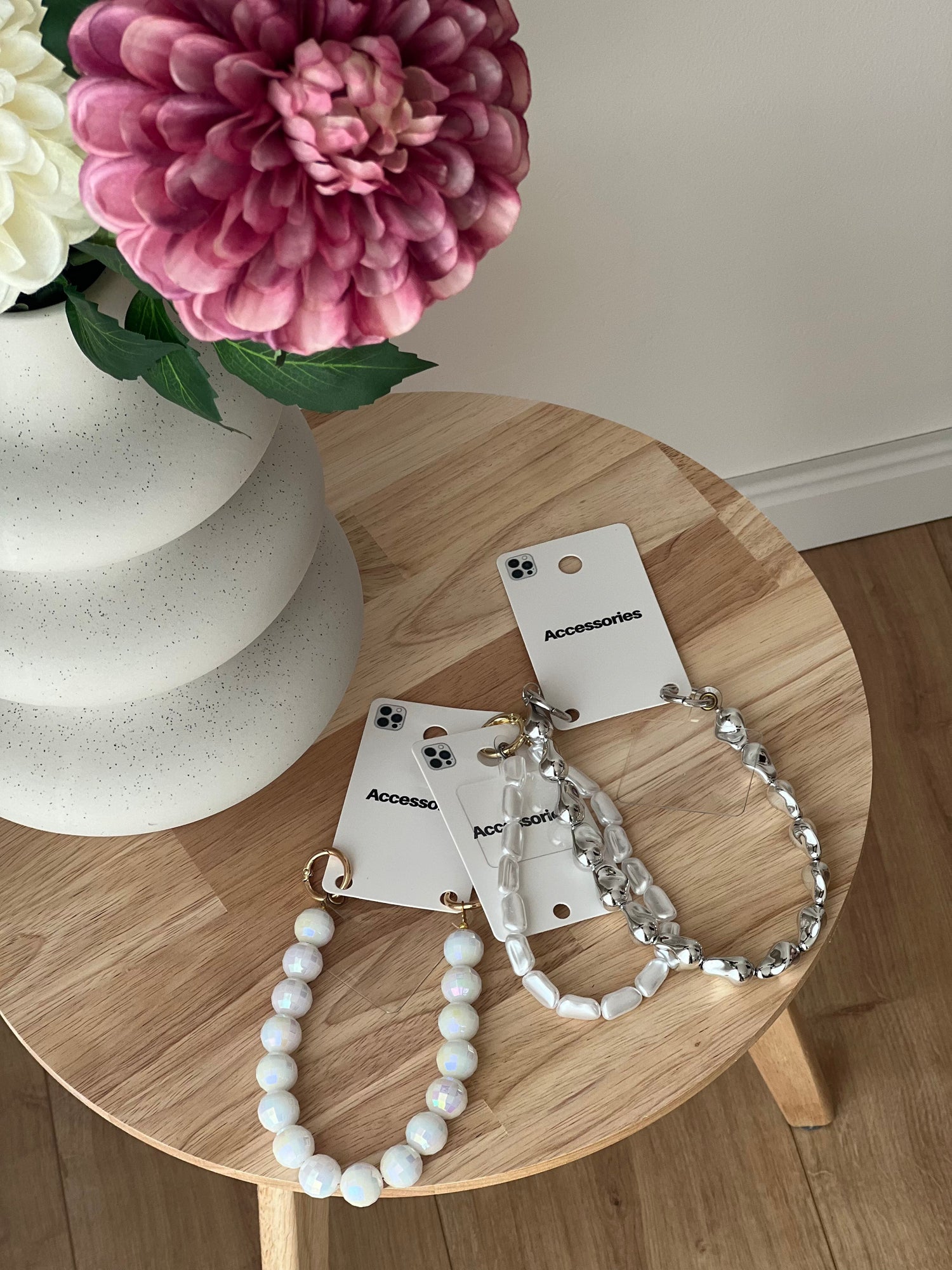 rei Handyketten von Dutch Atelier liegen auf einem Tisch neben einer Vase mit Blumen – stilvolle, minimalistische Handyketten Accessoires für Damen.