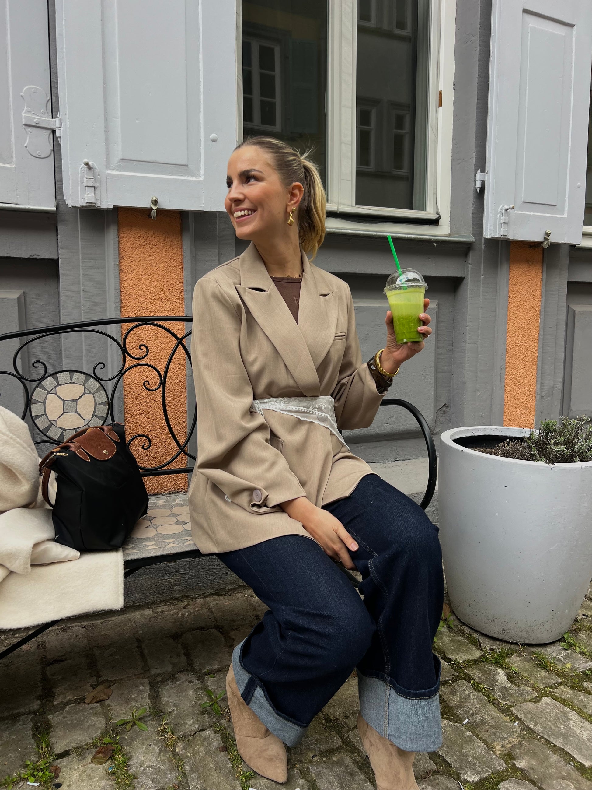 Yarah Blazer, Model Dutch Atelier, sitzt mit einem Smoothie auf einer Bank